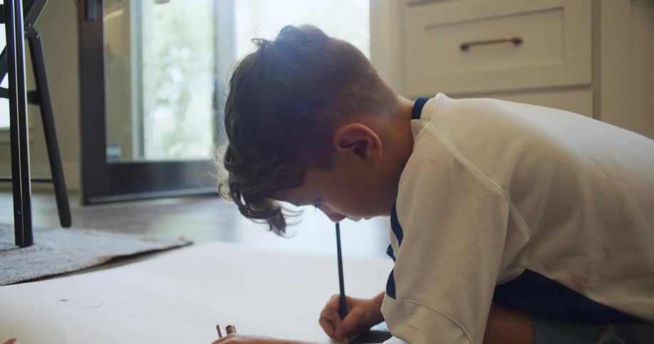 Boy sitting on floor at home draws on large paper