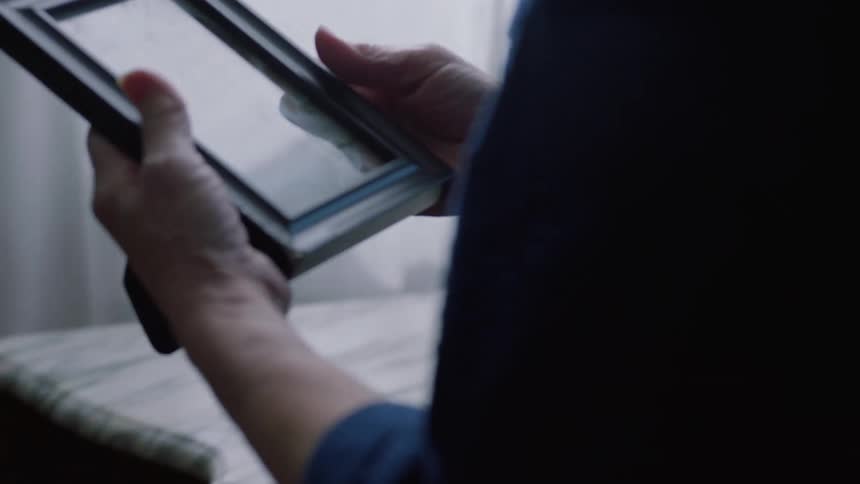 Elderly person takes a framed portrait from a table in the living room