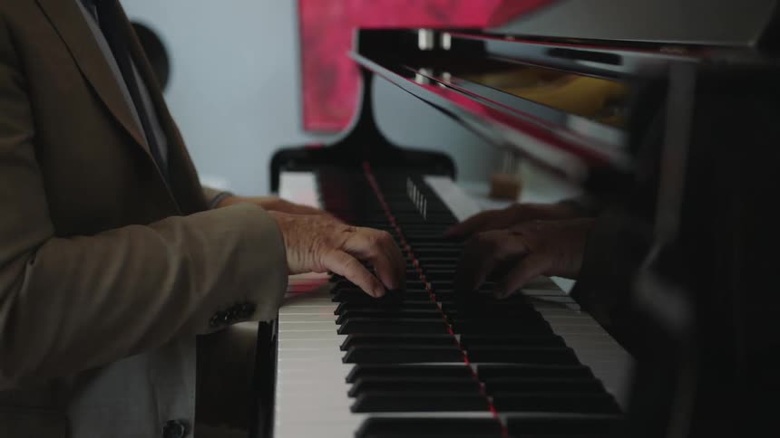 A man plays a piano wearing a suit and tie