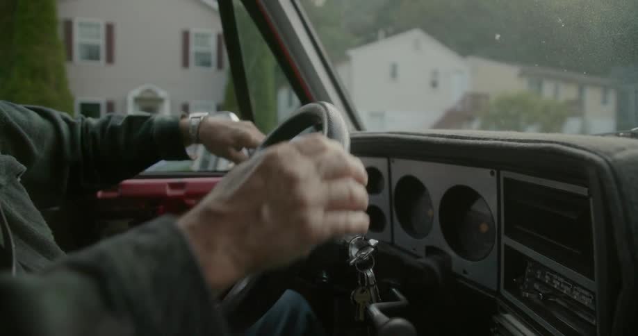 A man holds the steering wheel of his automobile and switches hands as he drives through a neighborhood