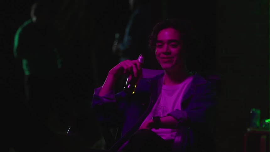 A man holding a beer sits in a bar and laughs and talks with someone