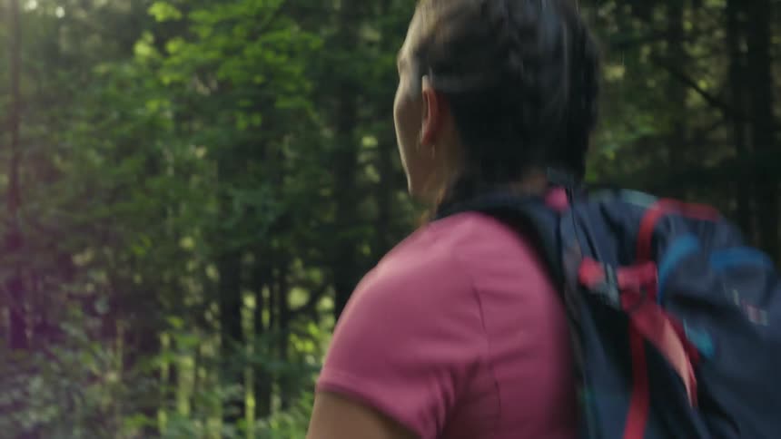 A girl with pigtails and wearing a backpack is walking through the woods
