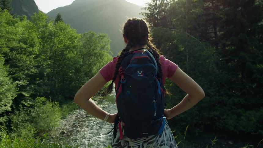 A hiker gazes at the landscape while standing near a stream in the countryside during the day
