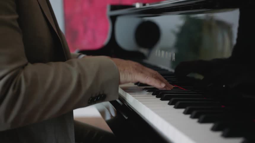 Glossy surface of piano reflects pianist wearing suit as he plays