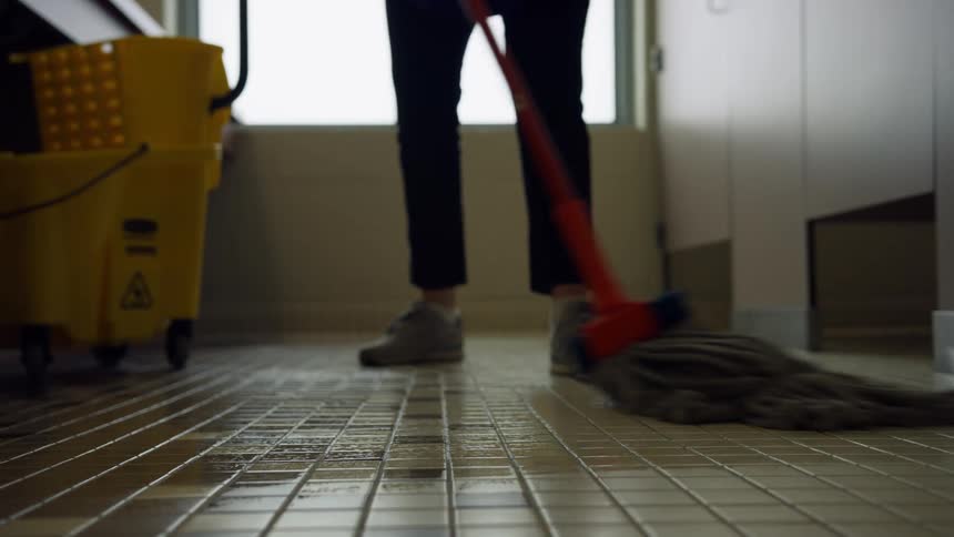 A custodian mops the floor of a public bathroom