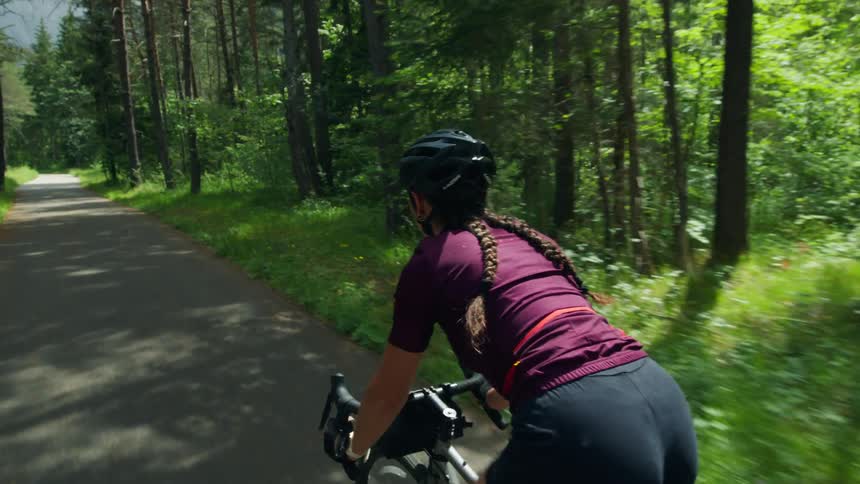 Woman cycles along narrow paved road through woods