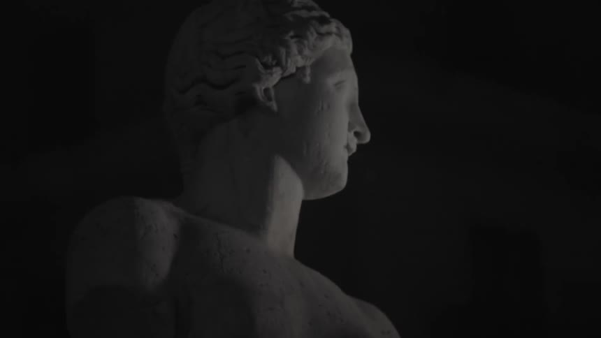 A stone statue of a man comes into focus in a dark area