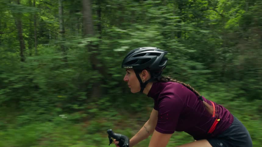A young white woman is riding a bike down the road in the forest area