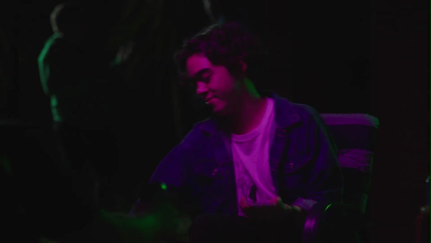 A young teenage boy is sitting down at a party and drinking a beer
