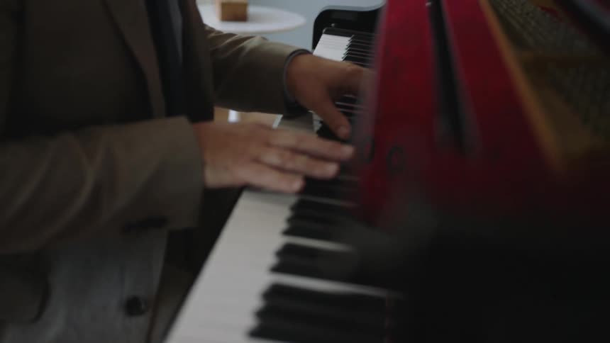 A man is sitting down playing a piano as his fingers press they keys