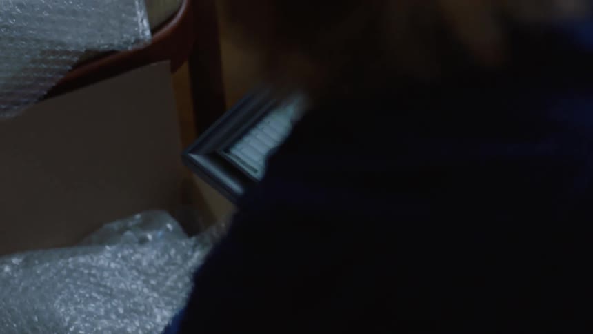 A woman admires a framed photograph before wrapping it in bubble wrap