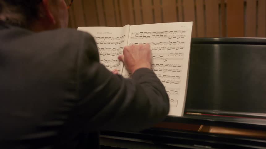 An older white man is playing the piano and reading off music on a piece of paper