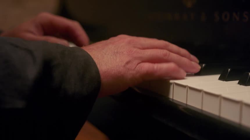 Man wearing a long sleeved outfit sits at piano playing