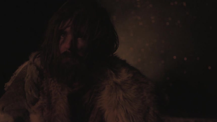 Bearded man in animal fur sitting near a fire at night