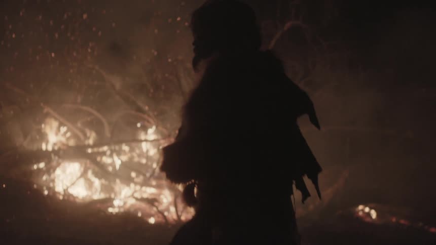 Bearded man in the wilderness walking in front of a fire
