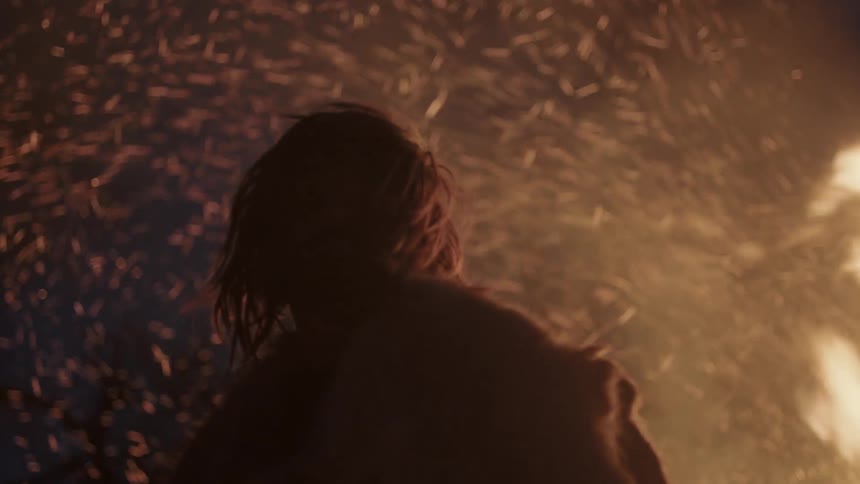 A man in fur clothes is standing in front of a raging fire at night
