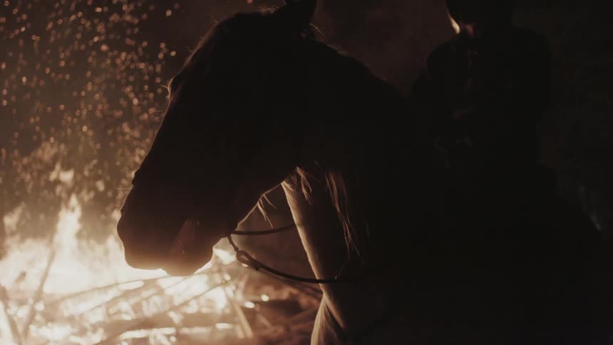 A stick carrying man rides horse beside fire