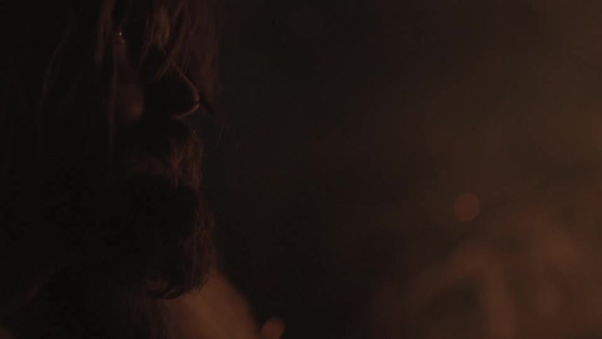 A man is standing at night facing a fire