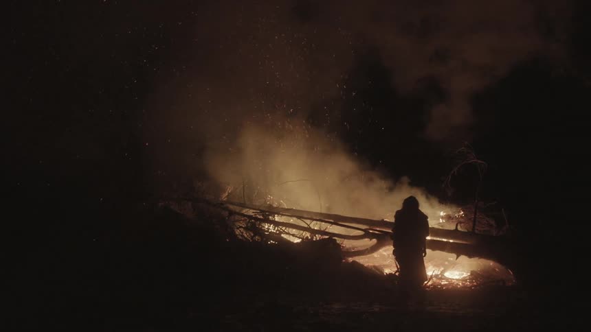 A person stands beside a burning pile of brush