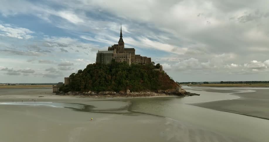 A person walks on the beach in front of a large building on an island