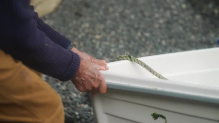 A man pushes a rowboat through gravel