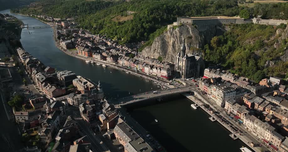 A town lining either side of a river at the bottom of a verdant valley during the day