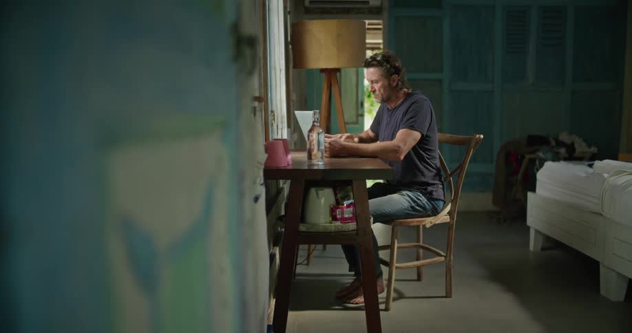 A man is sitting at a table in a room typing on a laptop computer