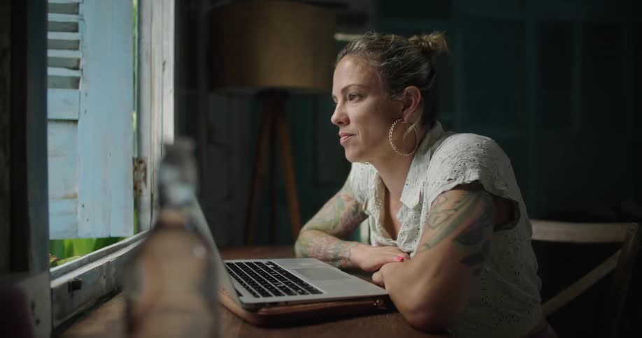 A woman is typing on the laptop by the window