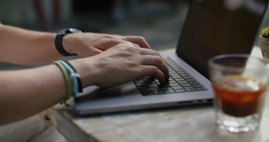 Man sitting on a cafe typing on he keyboard of a laptop