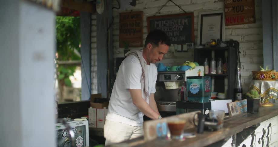 Waiter prepares coffee on an espresso machine on an outdoors tropical restaurant
