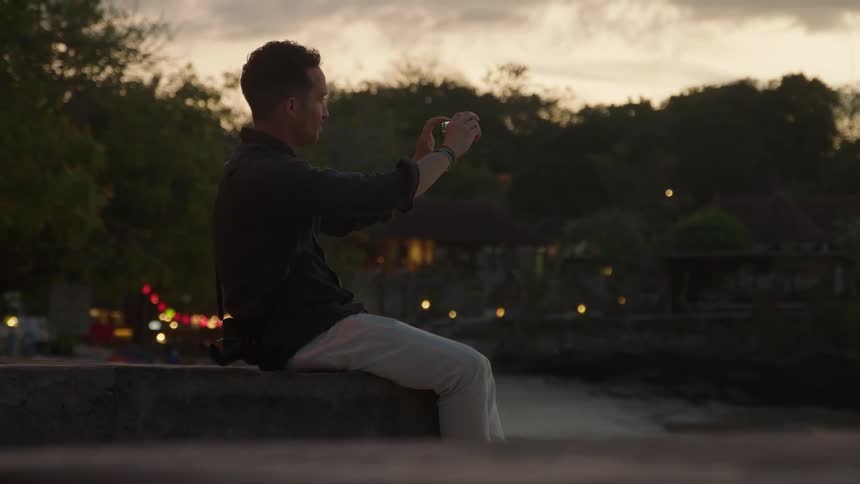 The man takes a picture of the river with his cell phone
