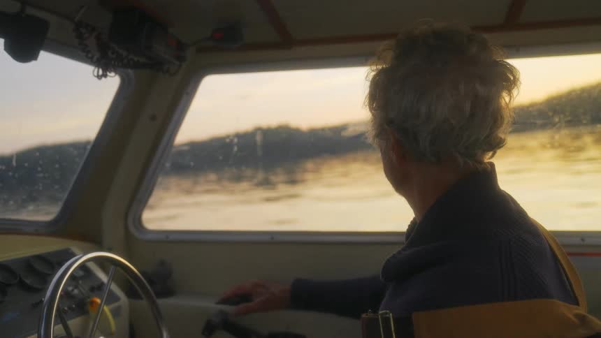 Elderly man drives a boat on a lake at evening