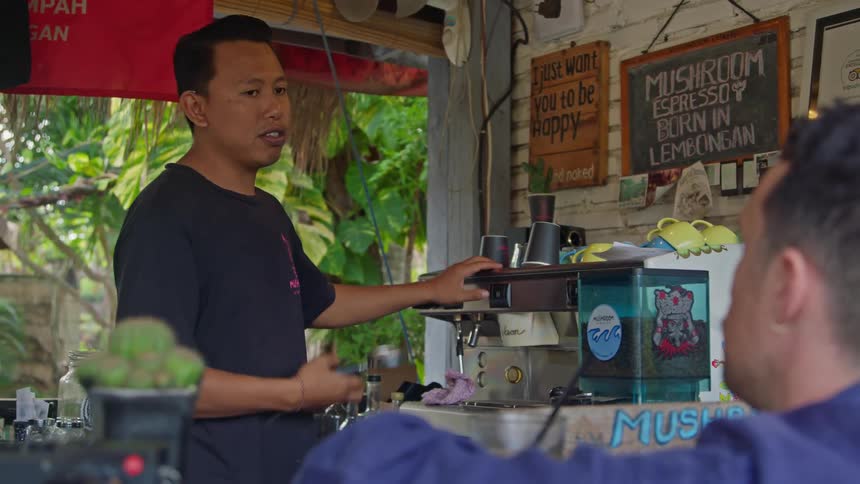 Restaurant owner prepares coffee on an espresso machine for a customer on an outdoors tropical restaurant