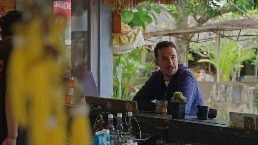 A man sitting at the counter of an outdoor bar smiling and talking