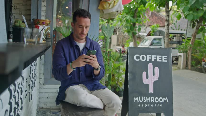 A man is using his phone outside by the coffee shop