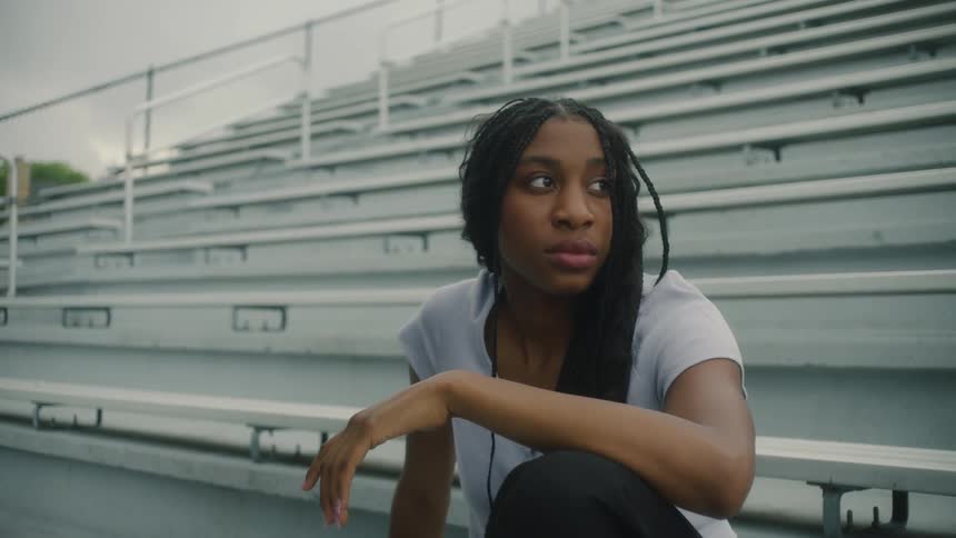 A teenage girl is sitting alone on empty bleachers looking around