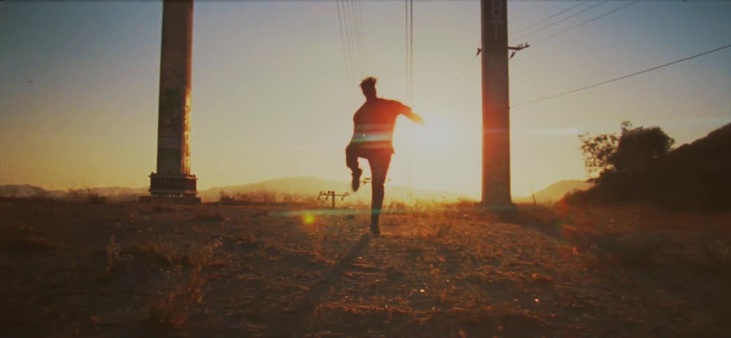 A man dances outdoors in a dusty field in the evening
