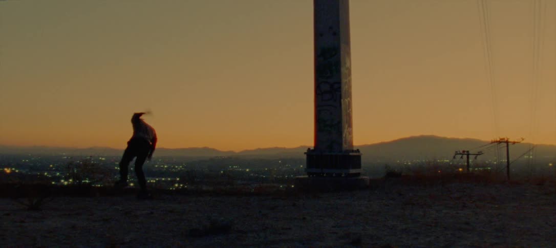 The silhouette of a young man dancing on a ridge above city lights against a golden sky