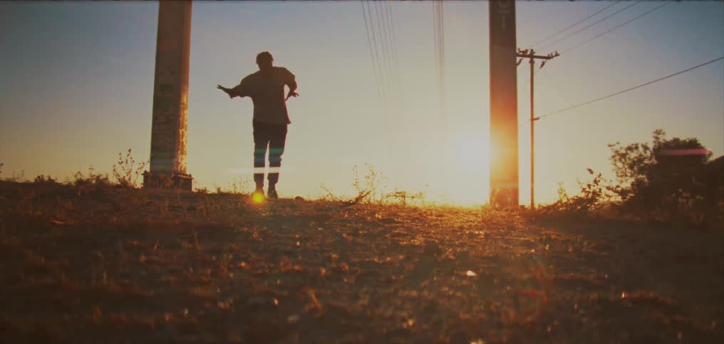 Sun shines behind the silhouette of a man dancing between two poles in the countryside at sunset