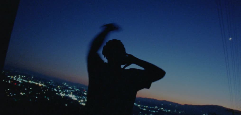 Silhouette of a young man dancing on the countryside near a town at evening