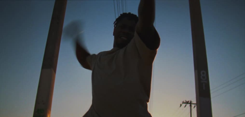 A man looks into the camera while dancing outdoors during the day