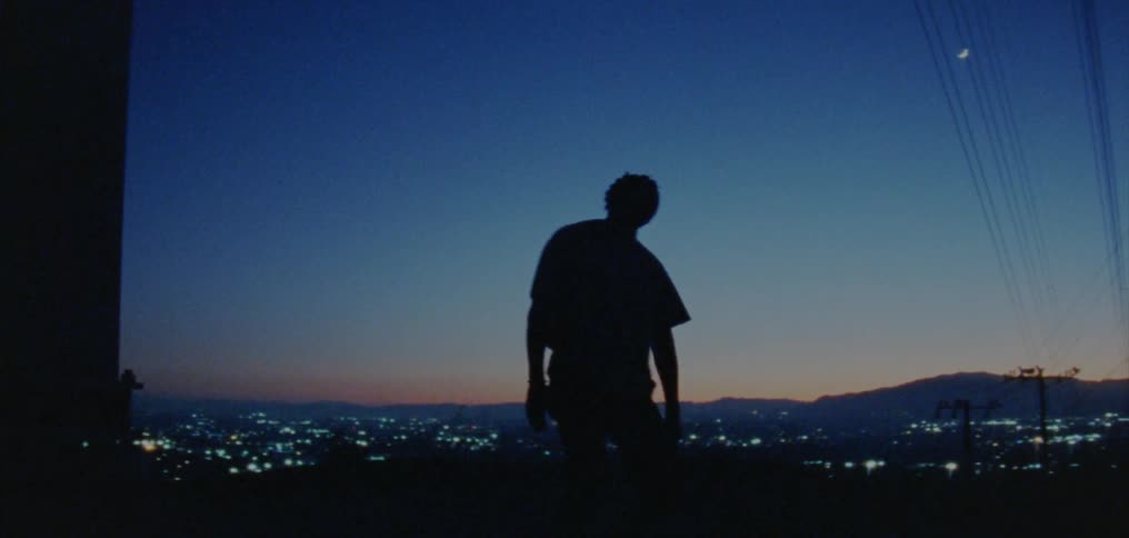 Silhouette of a young man dancing on the countryside near a town at nightfall