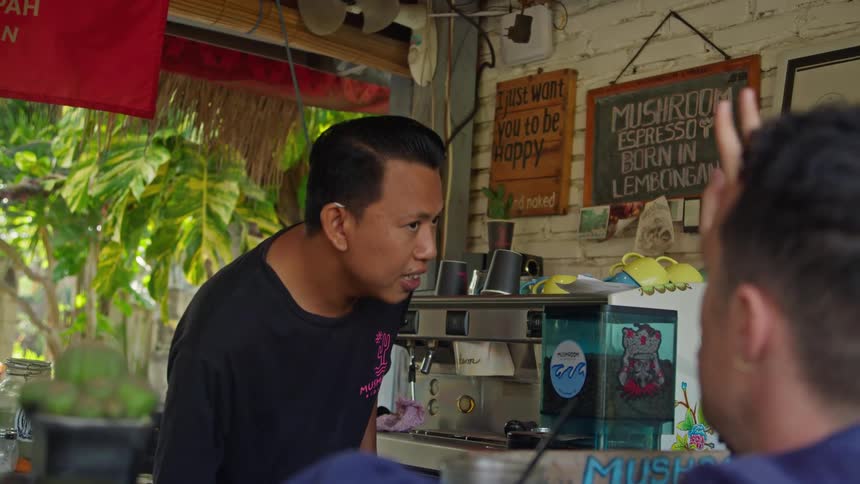 Waiter prepares a coffee on an espresso machine for a customer on a tropical outdoors restaurant