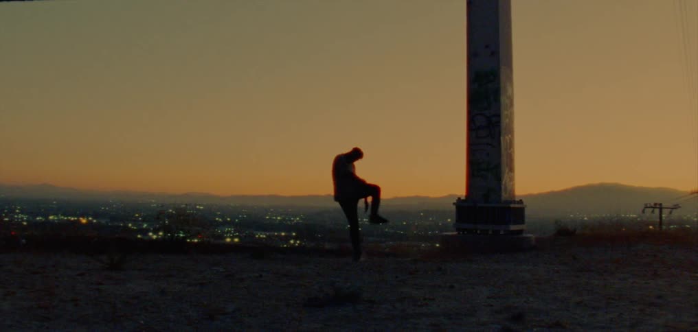 The silhouette of a man dancing joyfully on a ridge overlooking city lights against a golden sky