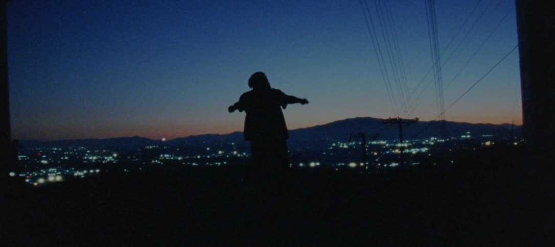 Male dancer silhouetted against city scape at night dances between support columns as red tints the horizon