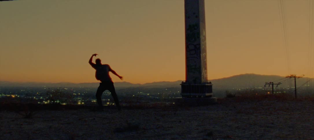 Silhouette of a young man dancing on the countryside near a town at evening