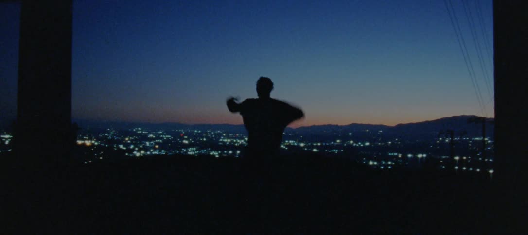 Silhouette of a young man dancing on the countryside near a town at nightfall