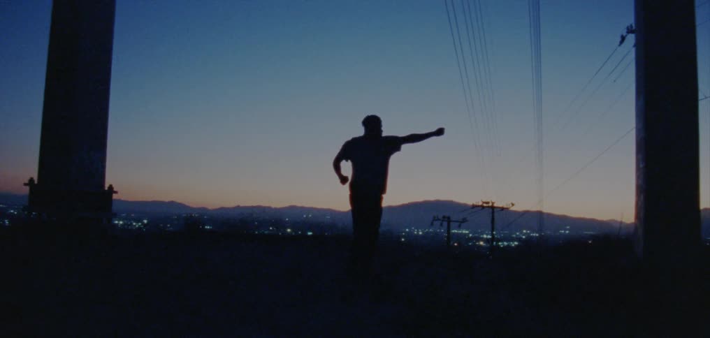Silhouette of a young man dancing on the countryside near a town at evening