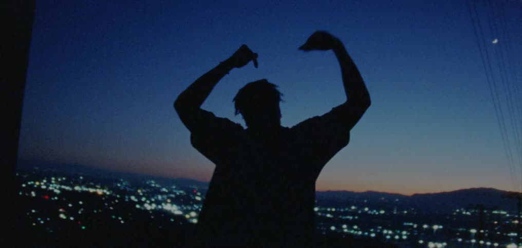 Male dancer silhouetted against city scape dances near power line pole