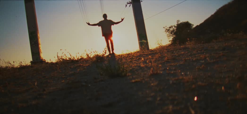 The sun shining and glaring behind a young man standing on a ridge with arms outstretched